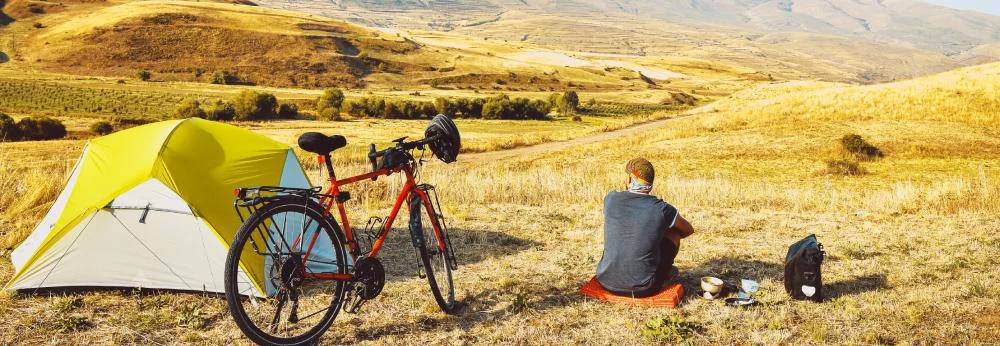 Person mit Fahrrad und Zelt in Gebirgslandschaft